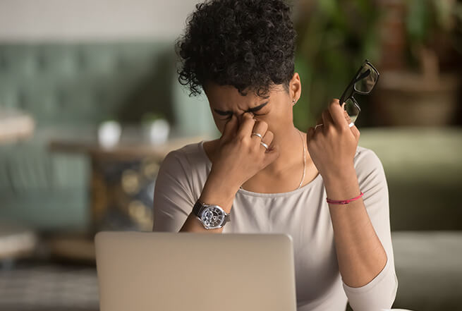 Woman pinching nose between eyes, straining from symptoms of dry eye.